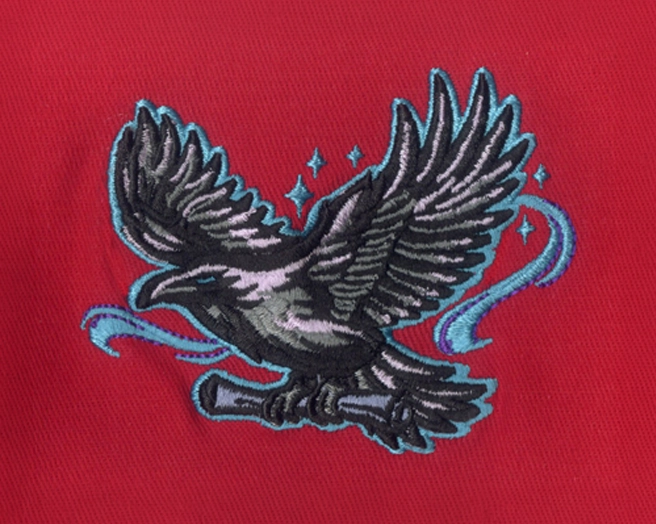 Embroidered patch of a black raven in flight outlined in cyan and purple thread on red fabric.