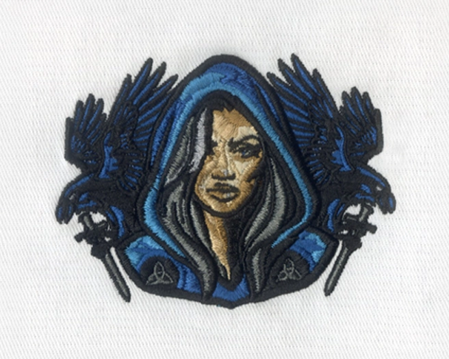 Embroidered patch of a hooded female figure flanked by two black ravens perched on daggers.